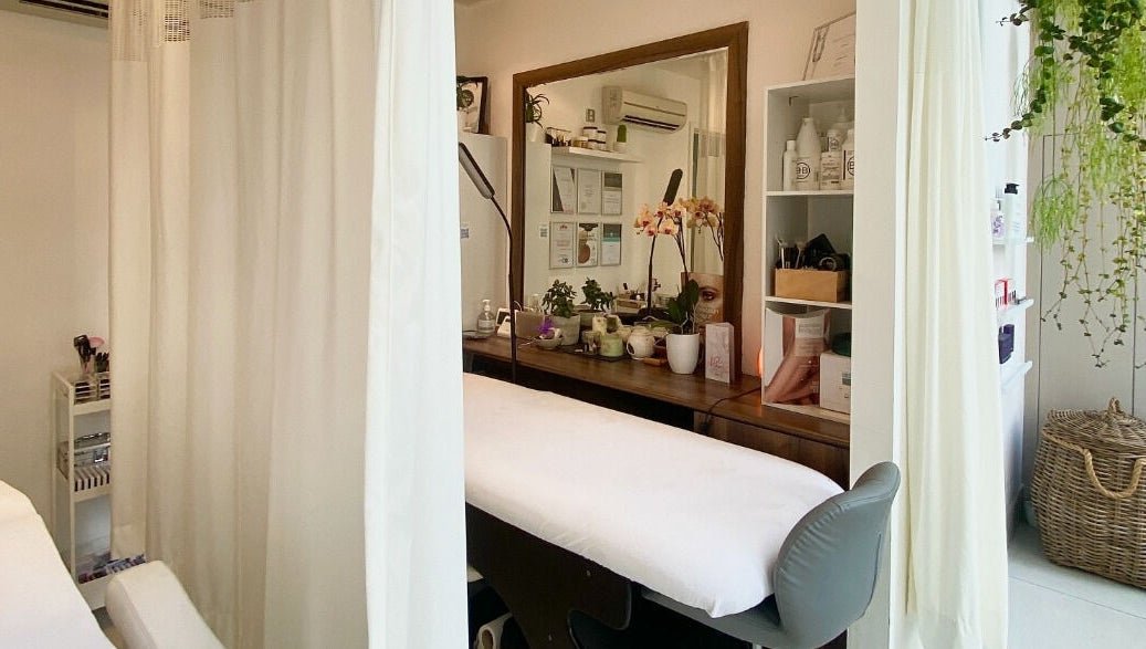 Linh Beauty's light-filled treatment room, with white curtains, plants and a treatment bed